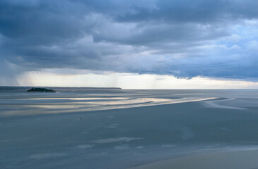Distant rain patches on the horizon over a serene tidal zone at dusk during low tide