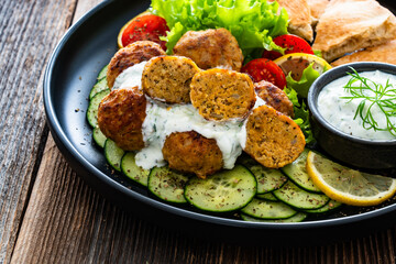 Fried meatballs with tzatziki sauce and pita bread on wooden table. Greek style food