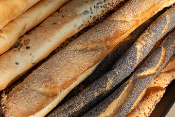  Assortment of freshly baked baguettes and bread rolls, featuring various toppings like poppy...