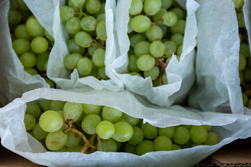 A close-up, top-down view of multiple punnets of fresh, bright green grapes, carefully packed with protective paper in a cardboard box, ready for market or export