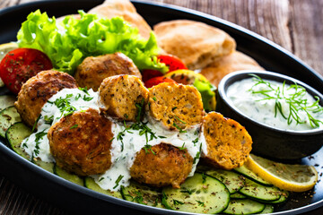 Fried meatballs with tzatziki sauce and pita bread on wooden table. Greek style food