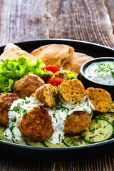 Fried meatballs with tzatziki sauce and pita bread on wooden table. Greek style food