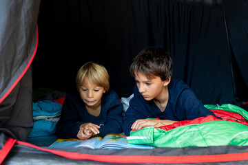 Children, siblings, enjoying a night in a tent in camping, laughing and reading books