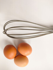 Three brown eggs and the tip of a whisk on a white background. Minimal and fresh — ideal for...