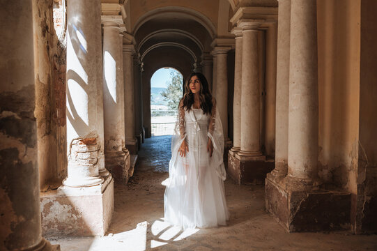 Bride in white gown standing in elegant stone corridor