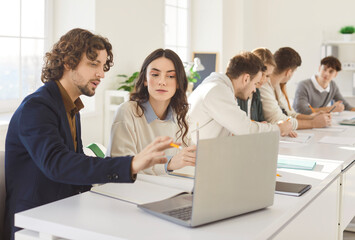 Young business coworkers, students using laptop online at work table, talking discussing project ideas for learning strategy, planning Internet startup, studying together, helping to explain 