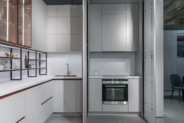 Fototapeta premium large modern built-in kitchen with lots of upper and lower cabinets, drawers and shelves. light countertop, beautiful wine glasses, glass doors, steel faucet and sink. luxury kitchen design.