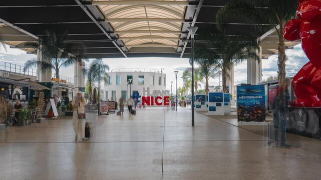 Timelapse of Nice Cote d'Azur Airport with people walking, palm trees modern architecture and I love Nice sign.