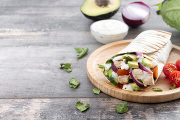 A delicious grilled chicken wrap with vegetables and avocado on wooden table. Copy space