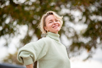 Smiling mature woman with hands on hips posing confidently in green turtleneck