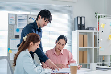 Obraz premium A professional group of Asian business people engages in a focused financial consultation and strategy discussion inside a modern office meeting room. With laptops open, financial charts displayed