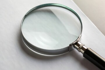 A magnifying glass resting on a blank sheet of white paper, highlighting its use for close examination.