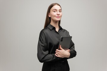 Confident Young Woman in a Sleek Black Outfit Stands With a Tablet, Exuding Professionalism and...