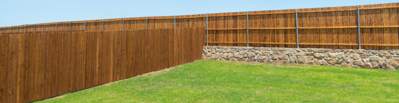 Panorama view stone retaining wall foundation, wooden fence in natural exterior wood stain, round fence post powder coating bracket of new construction home in Princeton, Texas, backyard privacy