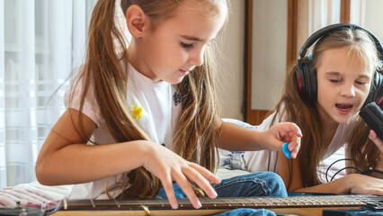 Little girl singing with microphone at home, concentrating, other child girl playing guitar.