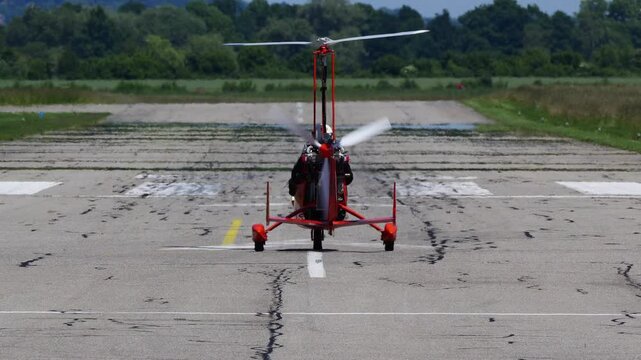 Footage of a red and black gyroplane or gyrocopter ready to take off from a runway