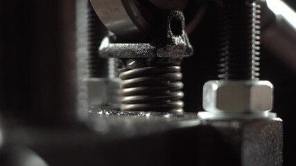 Vertical press spring compresses and decompresses repeatedly. Macro view shows shiny coils and metal bolts with dark blurred background. - Powered by Adobe
