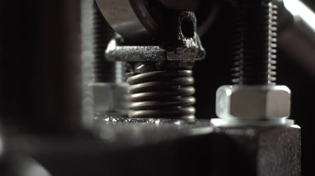 Vertical press spring compresses and decompresses repeatedly. Macro view shows shiny coils and metal bolts with dark blurred background.