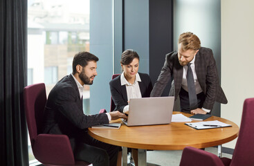 Team of business people working together with a laptop during a meeting or negotiation in the office. Teamwork and cooperation, focus, and collaboration in a professional work setting.