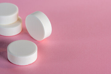 Four white medicine tablets standing on side and laying isolated on pink pastel background as macro...