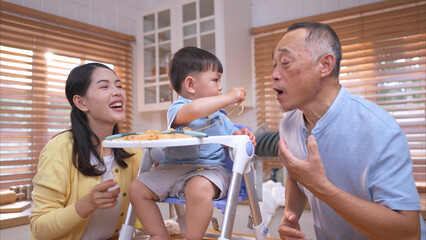 Happy Asian parents enjoying mealtime with their toddler in the kitchen
