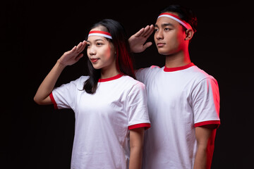 Portrait of Young Asian Man and Woman with Salute Gesture Wearing Red White Outfit, Indonesian Independence Day Concept 