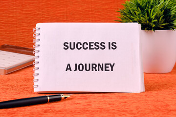 Concept text SUCCESS IS A JOURNEY on a spiral notebook on an orange background