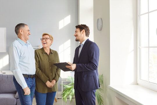 Happy smiling mature senior couple discussing with young man realtor real estate contract going to sign document. Elderly man and woman having consultation with financial advisor standing indoors.