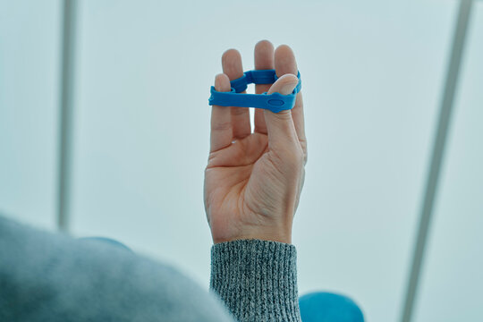man exercises his fingers with a blue elastic band