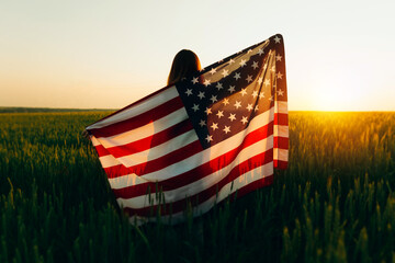 Young woman with American flag in a wheat field at sunset. 4th of July. Patriotic holiday, american...