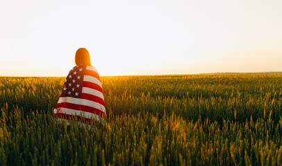 Young Woman with the American flag running in a wheat field at sunset. 4th of July. Independence...