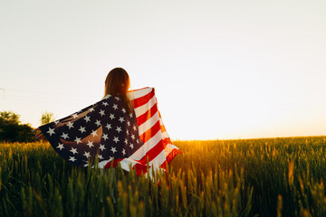 Young woman with American flag in a wheat field at sunset. 4th of July. Patriotic holiday, american...