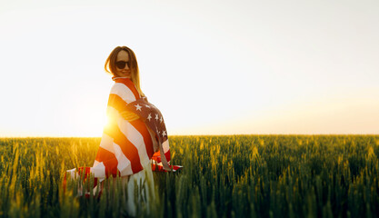 Young woman with American flag in a wheat field at sunset. 4th of July. Patriotic holiday, american...
