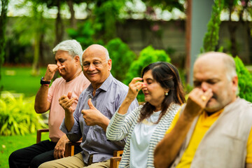 Indian seniors doing Pranayama in group while seated outdoors in garden with closed eyes