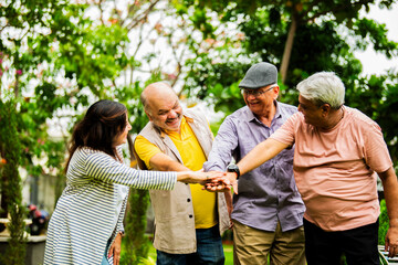 Seniors doing group huddle cheer standing outdoors in garden with happy and positive expressions