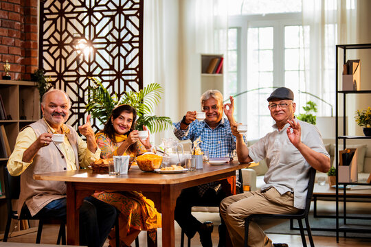 Seniors serving and eating together during happy indoor reunion around modern Indian dining table - Powered by Adobe