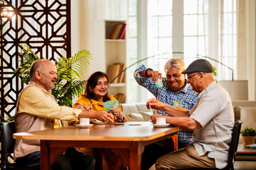 Indian senior citizens playing card game and bonding at cozy home dining table during reunion