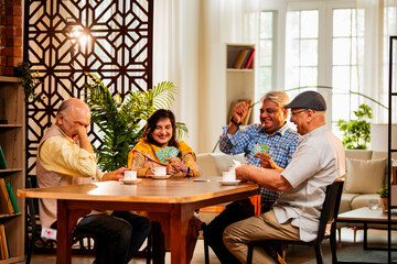Indian senior citizens playing card game and bonding at cozy home dining table during reunion