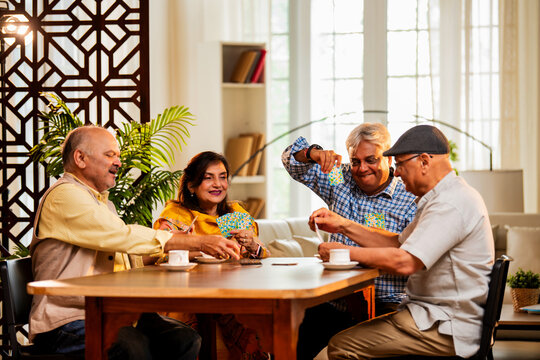 Indian senior citizens playing card game and bonding at cozy home dining table during reunion