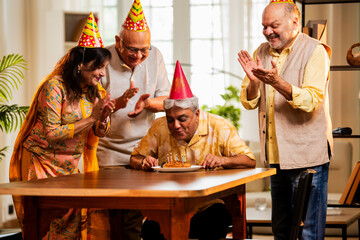 Indian senior adults cutting birthday cake and exchanging gifts during happy indoor celebration