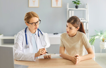 Focused female doctor, nurse looking at test result, discussing med anamnesis together with woman, concentrated medical professional engaged in thinking over treatment in hospital, clinic, talking 