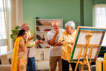 Senior artist painting as old friends enjoy indoor reunion time with praise and laughter