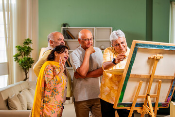 Senior artist painting as old friends enjoy indoor reunion time with praise and laughter
