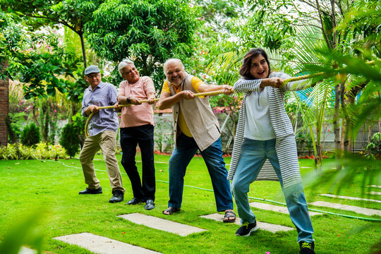 Senior playing tug of war outdoors, Indian old friends having fun in group reunion garden sport
