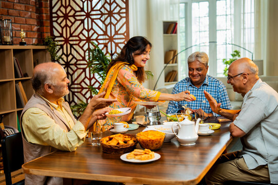 Seniors serving and eating together during happy indoor reunion around modern Indian dining table