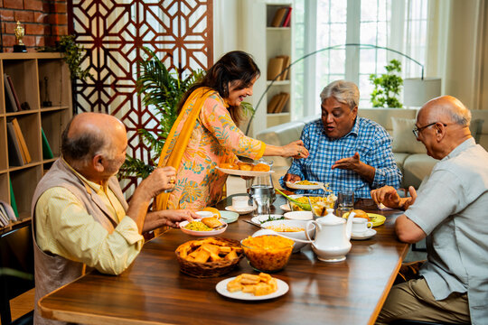 Seniors serving and eating together during happy indoor reunion around modern Indian dining table