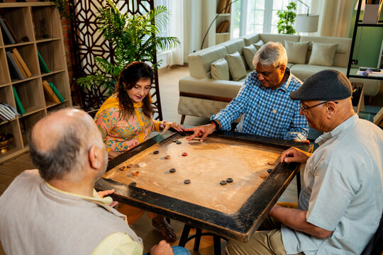 Indian retired adults playing carrom board game at dining table in cheerful indoor group activity