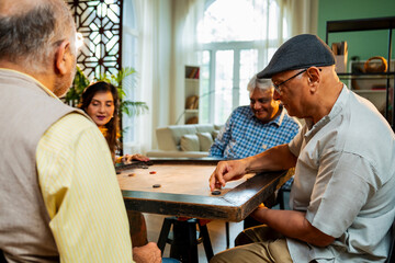 Indian retired adults playing carrom board game at dining table in cheerful indoor group activity