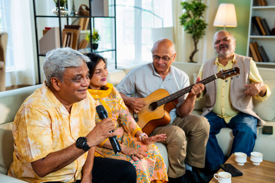 Senior group performing music indoors with guitar during joyful reunion on sofa at modern home