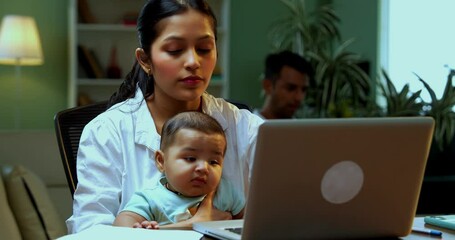 Indian mother multitasking with infant baby working from home on laptop and phone call with documents while father walks behind indoors, family, parenthood, young parents balancing work and care - Powered by Adobe